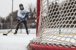 Person playing hockey on an ice rink with a close-up of the net in the foreground.